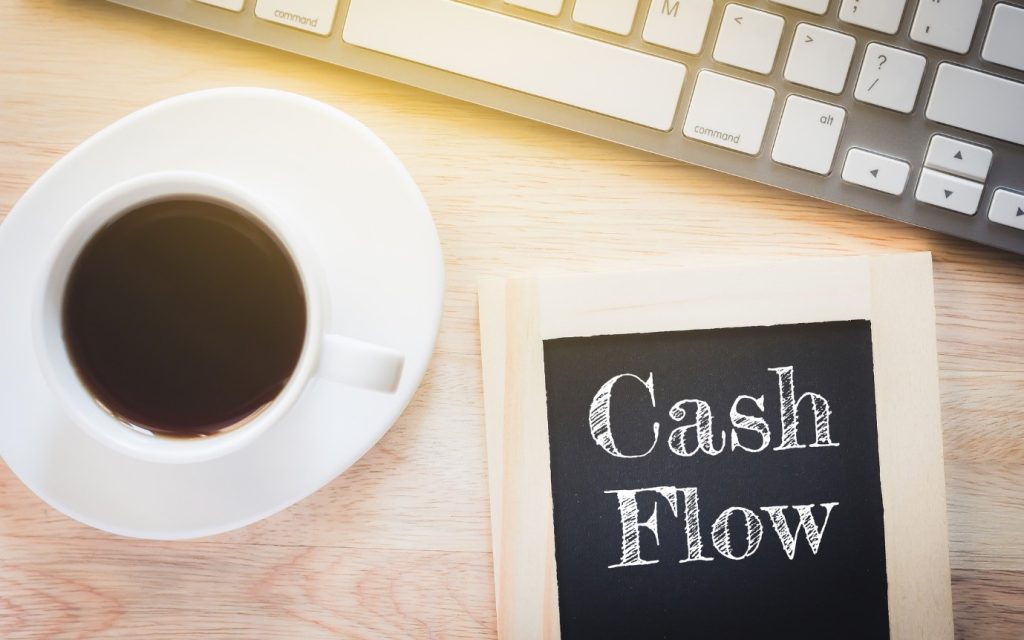 a cup of coffee besise a laptop with the word cash flow on the side