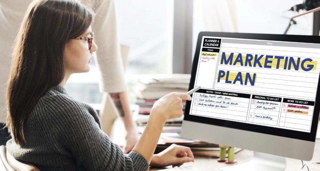 a lady in front of the computer pointing to a word marketing plan