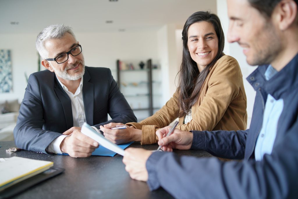 Attractive couple signing contract with real-estate agent in contemporary house