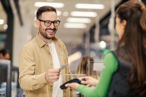 Un hombre feliz al pagar está pagando con tarjeta de crédito en pos terminal